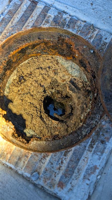 A cast iron drain opening scaled almost completely shut with rust and sediment