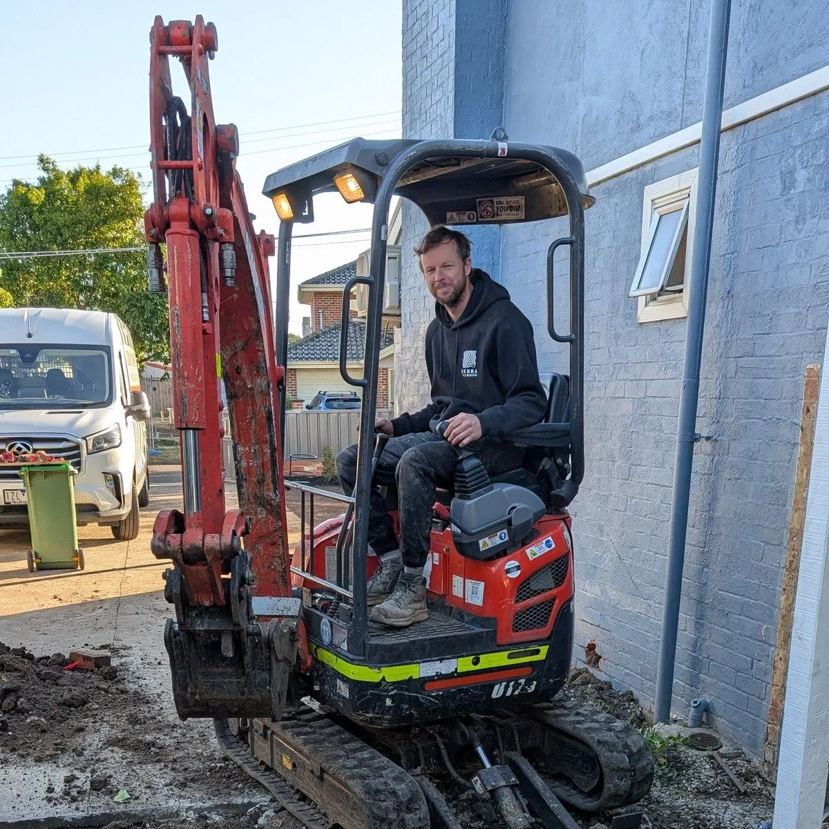 A Zebra Plumbing excavator opening up a deep drainage excavation beside a Melbourne home