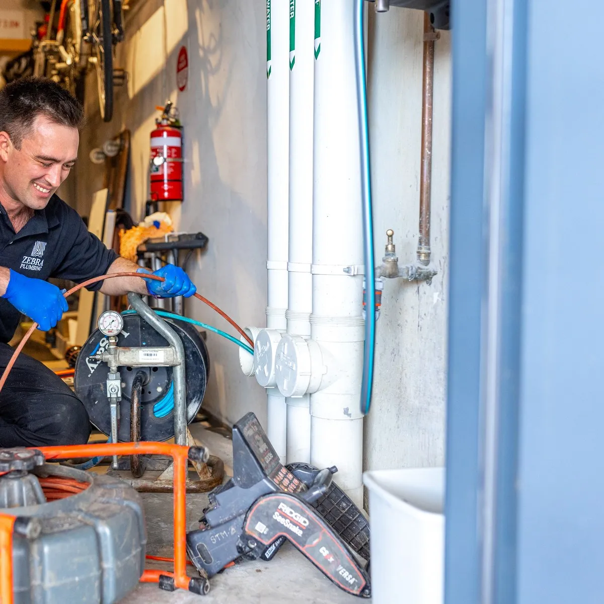 A Zebra plumber running the high-pressure jetter during a professional drain clean, camera gear alongside