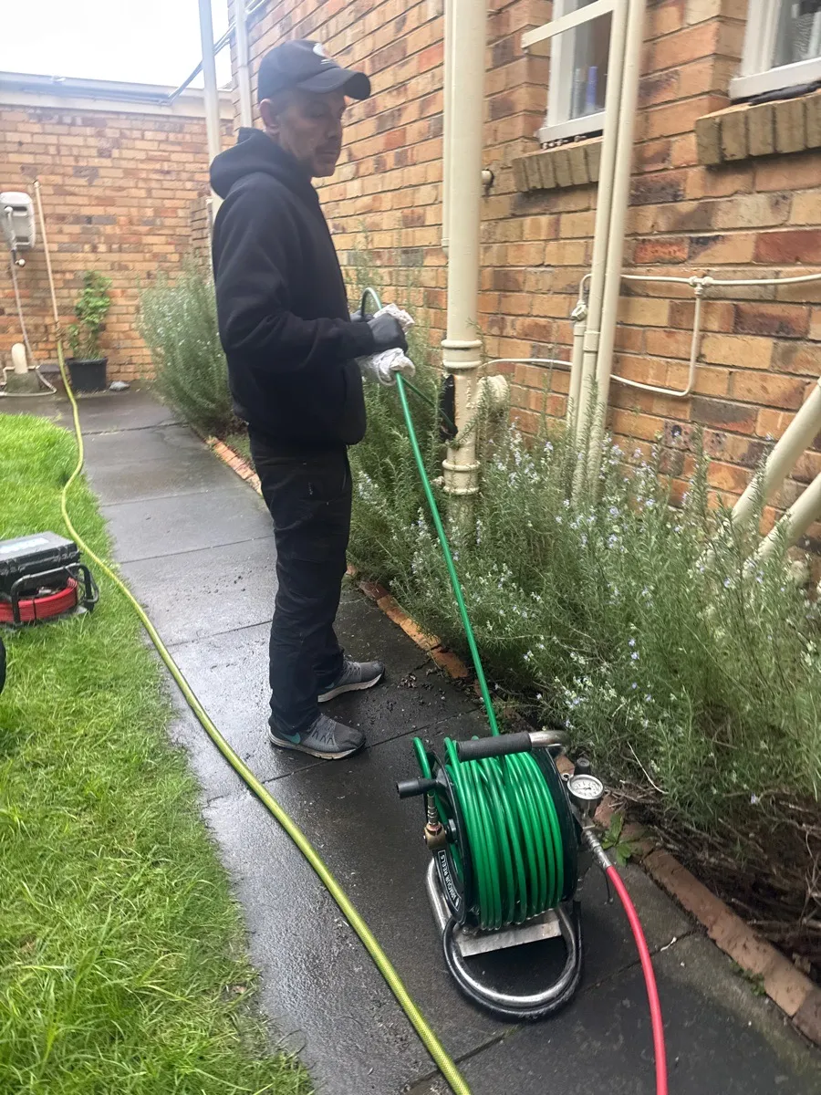 A Zebra plumber running the hydro jetter hose into an outside drain beside a brick house