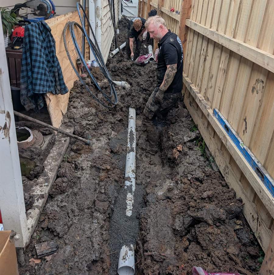 Two Zebra plumbers deep in the mud laying a new stormwater line beside a house