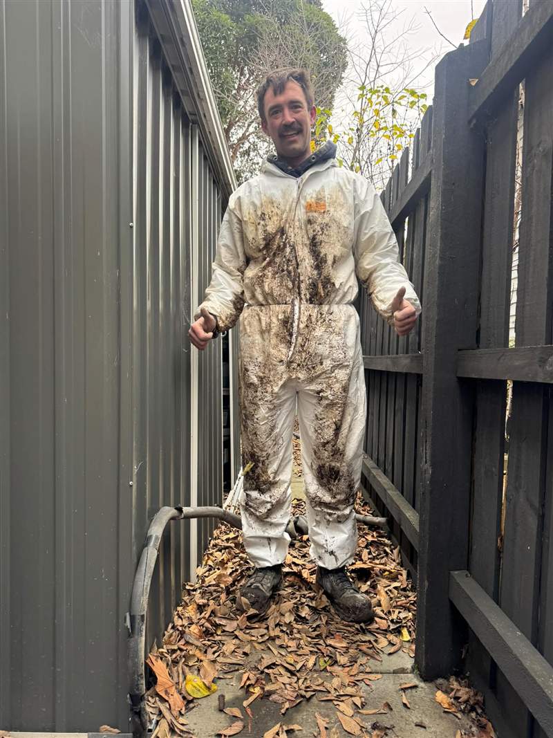 The same Zebra plumber in mud-covered coveralls after the under-house drainage work, thumbs up