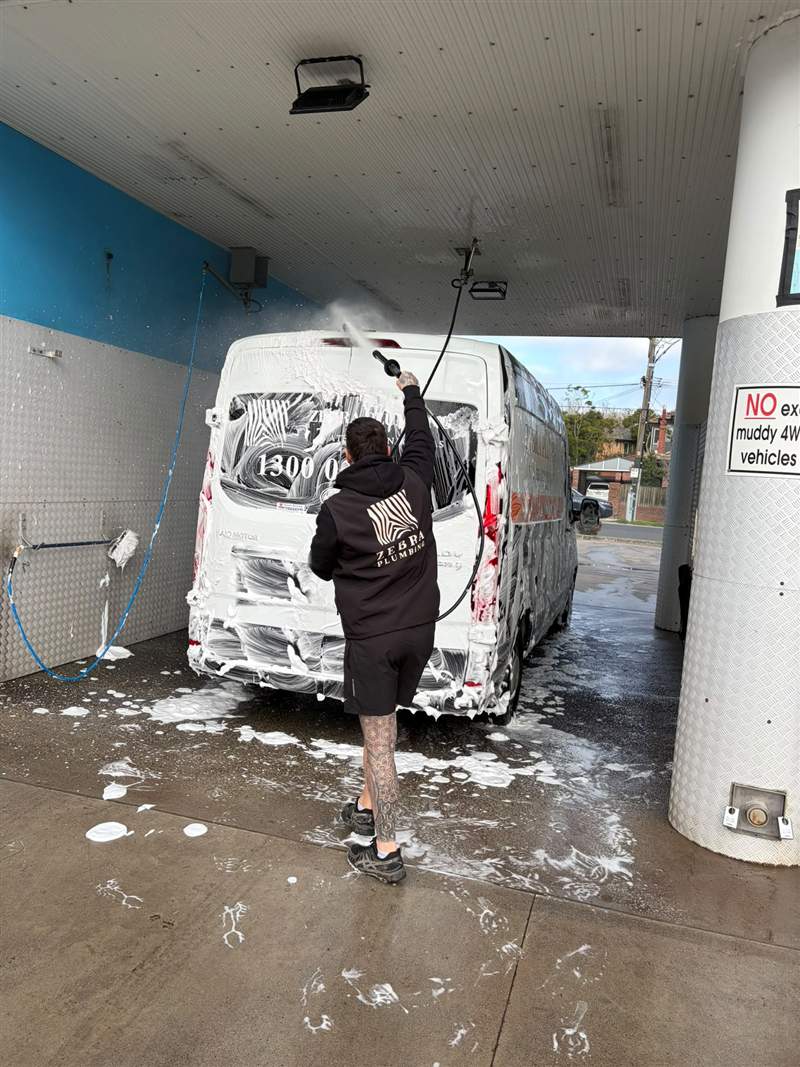A Zebra plumber pressure-washing the foam-covered Zebra Plumbing van after a muddy job